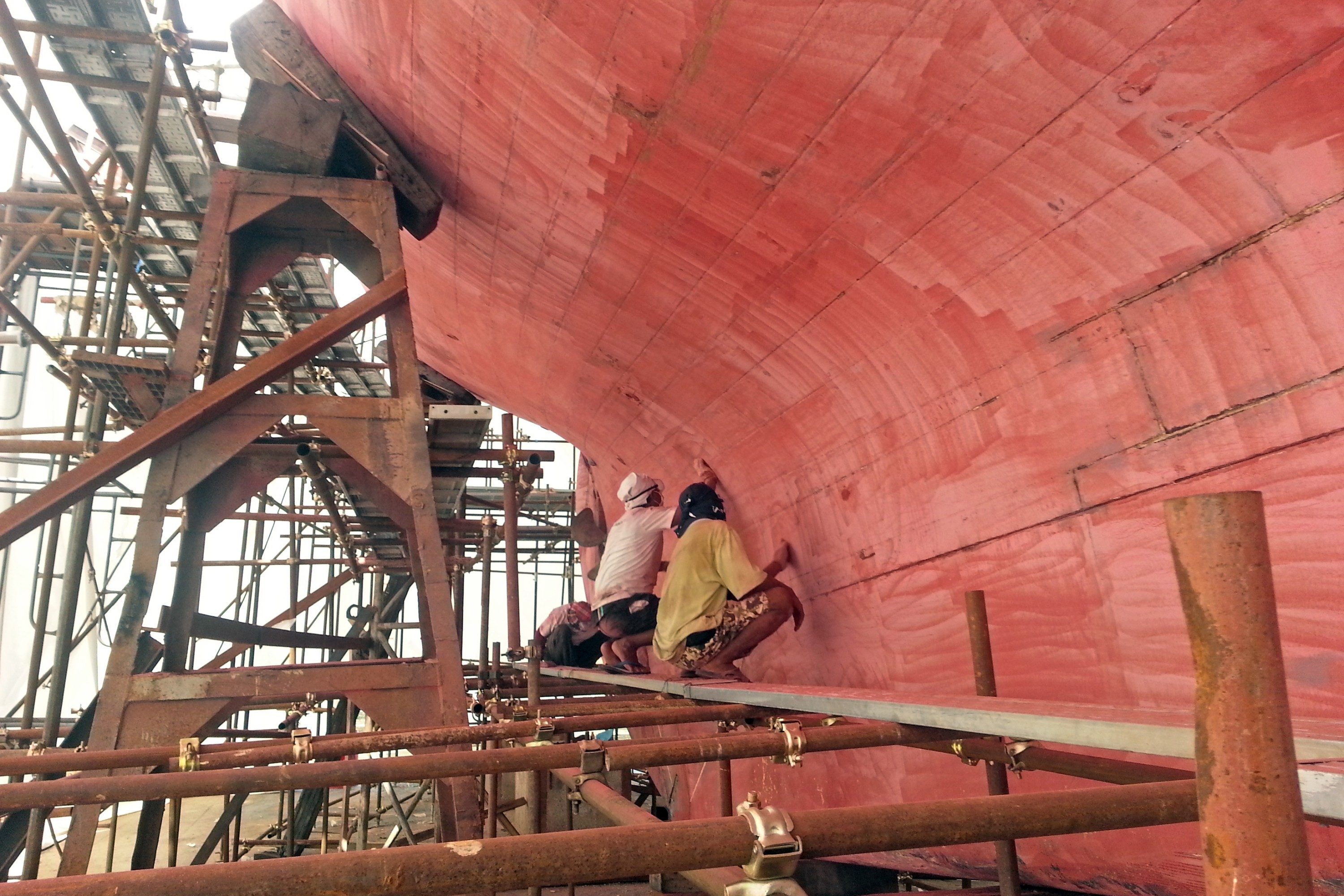 Dark blue hull and white superstructure inside a paint tent, with scaffolding along the topsides